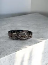 Cinto de cuero sintético con estampado de piel de serpiente y hebilla metálica plateada con detalles grabados de estilo western.