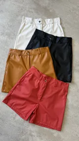 Short de cuero sintético color naranja, con bolsillos frontales y cierre de botón.