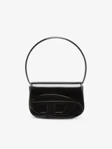 Bolso de hombro compacto, estilo bandolera, confeccionado en cuero negro con acabado espejado brillante. Presenta una solapa con placa oval D galvanizada en relieve y un asa de hombro curva. Incluye correa opcional para usar como bandolera.