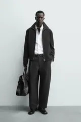 Sobrecamisa relaxed fit de Zara confeccionada en tejido negro con estructura diagonal. Presenta cuello subido, manga larga, bolsillos de vivo en la cadera y cierre frontal con cremallera.