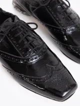 Zapato de cuero vacuno color blanco con acabado arrugado, diseño estilo oxford con detalles perforados, cordones y tacón bajo decorado con pedrería.