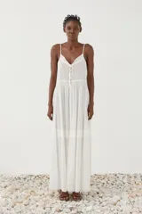Vestido largo blanco de breteles finos con escote en V, detalles de encaje y botones frontales. Cuenta con falda amplia de tejido liviano y semitransparente con bandas bordadas.