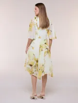 Vestido midi de gasa liviana con estampado floral en tonos amarillo y blanco, escote en V cruzado, mangas cortas amplias tipo capa, cintura entallada y falda con vuelo y ruedo irregular.