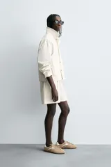 Shorts de algodón color blanco roto, de corte regular fit, con cintura ajustable mediante cinturón del mismo tejido y hebilla metálica. Presenta bolsillos delanteros y bolsillos traseros de vivo.