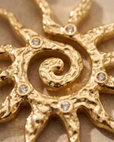 Collar de bronce con baño de oro, compuesto por una cadena fina y un dije colgante en forma de sol con textura irregular y detalles de circonitas incrustadas.