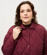 Campera acolchada de color bordó con diseño capitoneado de rombos. Presenta cuello camisero, cierre frontal con broches a presión y dos bolsillos frontales aplicados.