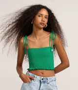 Blusa cropped verde con cuerpo fruncido en lastex, escote cuadrado y tirantes finos para anudar en los hombros. Detalle de pequeñas conchas marinas colgando en las puntas de los tirantes y terminación con volados en el ruedo.