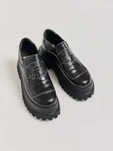 Mocasines de plataforma alta con diseño de estilo rebelde. Presentan un estampado de cuadros en tonos violeta y amarillo, confeccionados en lona con detalles en cuero. Cuentan con una suela robusta y elásticos laterales ocultos para facilitar el calce.