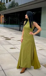 Vestido largo de corte recto y sin mangas, con cuello alto y una abertura lateral pronunciada en la falda. Presenta una textura suave tipo gamuza en color verde oliva.