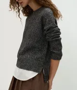 Suéter de punto jaspeado en color gris oscuro, con cuello redondo y mangas largas. Presenta un diseño integrado con una camisa blanca debajo, creando un efecto de capas superpuestas.