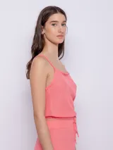 Top sin mangas de tejido texturado color coral, con tirantes finos y escote cuadrado. Presenta un ajuste holgado en la parte superior y un elástico ajustable en la cintura.