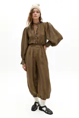 Pantalón de lino con diseño a rayas verticales en tonos tierra, de tiro medio y corte holgado. Presenta pretina con pasacintos, bolsillos laterales y traseros, y puños ajustados en los tobillos con botones de nácar.