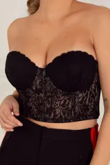 Corset corto negro de puntilla con copa y aro, forrado en tul. Espalda con cintas cruzadas de cetinete y breteles desmontables regulables.