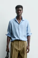 Camisa de corte relajado confeccionada en tejido fluido con mezcla de viscosa, color celeste. Presenta cuello solapa, manga larga con puños abotonados y cierre frontal de botones.