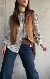 Chaleco de gamuza color camel forrado, con ribetes decorados con tachas metálicas y tiras colgantes con flecos en el lateral.
