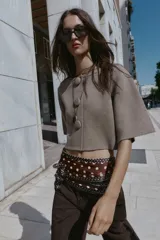 Chaqueta corta de punto color beige, con cuello redondo y manga tres cuartos. Cierre frontal con tres botones forrados a tono.