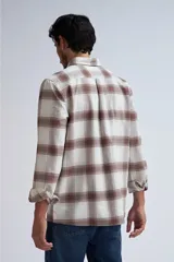 Camisa de manga larga a cuadros color beige y marrón, con cuello clásico, cierre frontal con botones a presión, dos bolsillos con solapa abotonada en el pecho y puños abotonados.