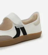 Championes estilo chutera de mujer, con diseño de punta redonda y cierre de velcro. Presenta una combinación de colores blanco, beige y negro con recortes contrastantes y suela plana color caramelo.