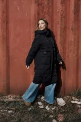 Campera larga acolchonada color marrón, con diseño midi, capucha amplia, cierre frontal con cremallera y broches, y bolsillos delanteros con tapa.