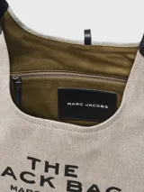 Cartera tipo hobo de Marc Jacobs, confeccionada en lona color beige con detalles en cuero negro. Presenta el logo estampado en el frente y una correa de hombro ajustable.