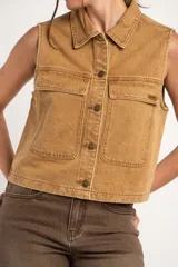 Chaleco de jean tostado con efecto lavado, cuello camisero, cierre frontal con botones metálicos y bolsillos delanteros con solapa. Diseño sin mangas y corte al cuerpo.