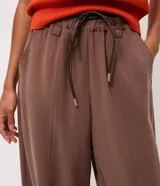 Pantalón carrot color marrón de modelado suelto en la cadera con barra afinada, cintura elástica con amarre ajustable y bolsillos.