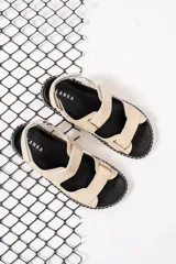 Sandalias planas color nude con tiras anchas con ajuste de velcro y suela negra con detalle de costuras blancas.