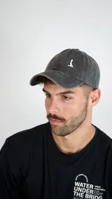 Gorra de béisbol color gris oscuro con efecto lavado, cuenta con un pequeño logo bordado en color blanco en la parte frontal y visera curva.