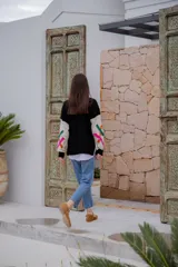 Sweater de punto color crudo con cuello redondo negro y bordados decorativos en forma geométrica en colores fucsia, verde y naranja. Tiene mangas largas con puños negros.