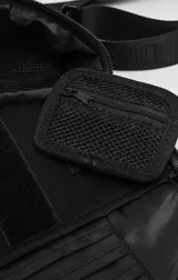 Bolso circular de estructura rígida, color negro, diseñado para el transporte de auriculares y accesorios. Cuenta con manija superior reforzada, correa de hombro ajustable con logo grabado, cierre perimetral y bolsillo trasero de acceso rápido.