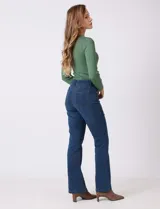Jean de tiro alto con corte bootcut, ajustado en cadera y muslos con una sutil apertura desde la rodilla. Presenta diseño clásico de cinco bolsillos, cierre con botón y costuras en contraste. Su diseño posterior incluye costuras estratégicas para un efecto de realce en la silueta.