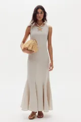 Vestido largo de lino color beige, sin mangas, con cuello redondo y diseño ajustado que se ensancha en la parte inferior con godets que aportan movimiento al ruedo.