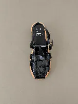 Sandalias de cuero charol color negro, estilo romano o pescador, con múltiples tiras entrelazadas en el empeine, suela plana de madera clara y tira ajustable con hebilla metálica en el tobillo.