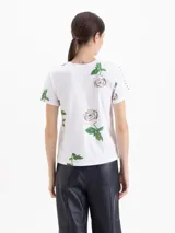 Remera de algodón blanca con estampado de rosas, cuello redondo, mangas cortas y detalle de tachas metálicas en los hombros.