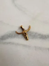 Dije con forma de cráneo de toro en color dorado, fabricado en acero quirúrgico hipoalergénico.