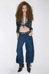 Jean de tiro medio-alto con calce holgado y relajado. Presenta piernas amplias con recortes curvos que se estrechan hacia el tobillo, creando una silueta tipo barril. Confeccionado en denim rígido color azul con sobreteñido negro, cuenta con cierre, botón y bolsillos traseros desplazados hacia el frente.