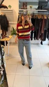 Sweater tejido de punto con diseño a rayas horizontales en tonos amarillo, celeste y marrón. Presenta un cuello polo con escote en V, mangas largas y un corte holgado.