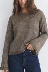 Sweater de tejido de punto con acabado brillante de lurex, color visón. Presenta cuello redondo, mangas largas acampanadas y terminaciones con detalle de puntilla tejida en el ruedo y los puños.