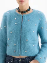 Cardigan de tejido de punto suave en color azul, con cuello redondo, cierre frontal y manga larga. Presenta pequeños apliques metálicos en forma de corazón distribuidos por toda la prenda.