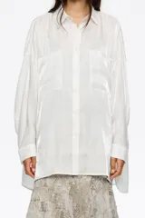Camisa oversize de manga larga, color blanco, confeccionada en viscosa brillante. Presenta cuello camisero, cierre frontal de botones y dos bolsillos de parche en el pecho.