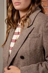 Chaqueta de corte sastre en color marrón con textura jaspeada, diseño de doble botonadura con cuatro botones frontales, solapas clásicas y bolsillos con solapa.