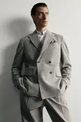 Blazer regular fit de Zara, confeccionada en tejido con mezcla de lana y algodón con diseño de cuadros grises. Cuenta con solapas de pico, doble botonadura cruzada, bolsillos con solapa en la cadera y bolsillo de vivo en el pecho.