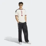Camiseta de fútbol Adidas del Manchester United, correspondiente a la tercera equipación. Es de color blanco marfil con detalles en bordó y negro en el cuello, puños y hombros. Cuenta con el logotipo de Adidas, el escudo del club y un gráfico alineados verticalmente en el centro del pecho.