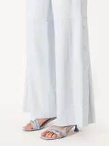 Pantalon de cuero de corte ancho y tiro medio, con cintura elástica y detalle de botones a presión en los laterales de las piernas.