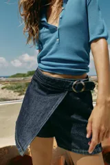 Falda pantalón cruzada de denim en color celeste, con diseño cruzado al frente, cierre frontal oculto y hebilla decorativa redonda en la cintura.