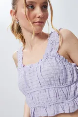 Top sin mangas lila elastizado y texturizado con volados en breteles y escote.