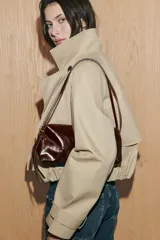 Bolso de hombro tipo baguette en color negro con acabado brillante. Presenta un diseño rectangular con cierre de cremallera superior y doble asa ajustable mediante hebillas metálicas.