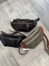 Riñonera de cuero color negro, con múltiples compartimentos con cierre metálico, detalles de tachas en los laterales y correa regulable.