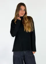 Sweater de cuello alto en color beige, con diseño de punto liso y terminaciones acanaladas en puños y ruedo. Presenta aberturas laterales en el bajo y un detalle de borde desflecado en el ruedo y los puños.
