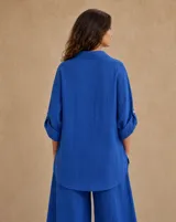 Camisa de lino color azul francia, de corte holgado, con mangas largas regulables, bolsillo ojal en el pecho y botones de nácar en la parte frontal.
